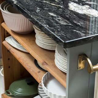Kitchen storage, wooden shelves below a marbled worktop stacked with plates, dishes and casserole dishes
