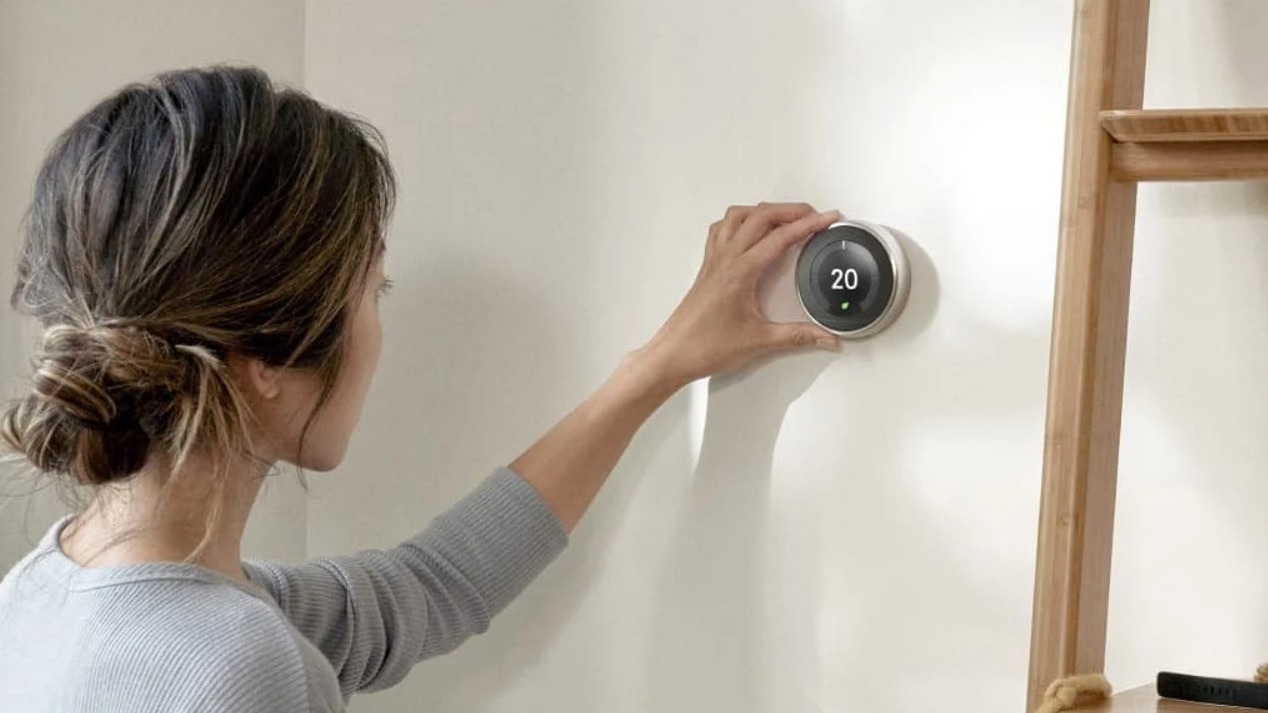 The Nest Learning Thermostat mounted on a wall being controlled by a woman