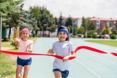 A small girl runner crossing finish line in a race competitive in nature.