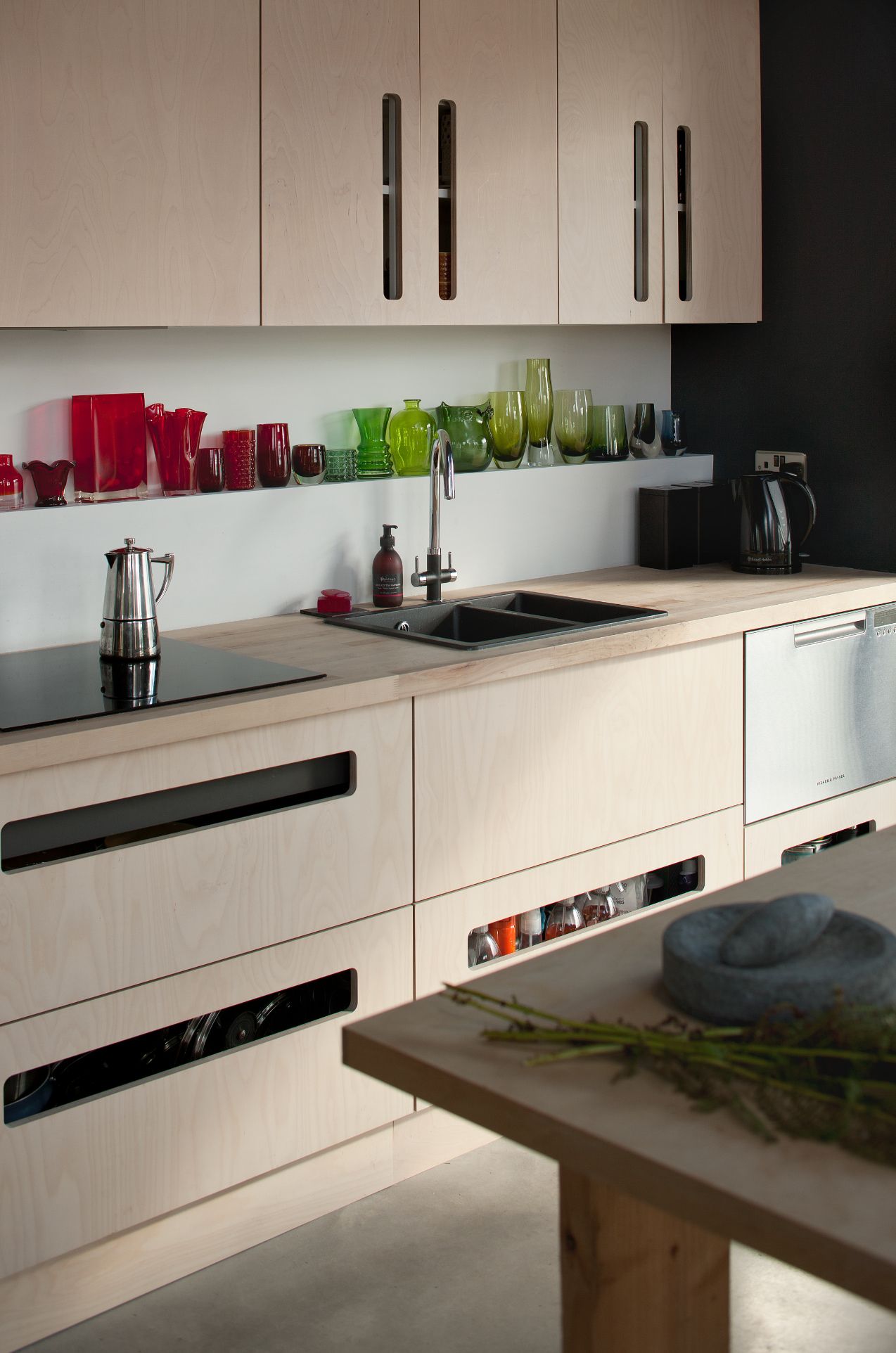 A kitchen with plywood fittings and multicoloured glass on. a shelf above the backsplash
