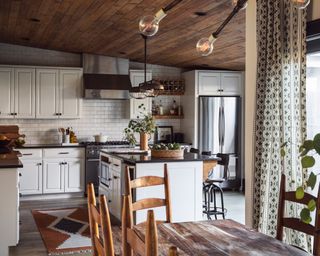 kitchen diner with wooden ceiling, white cabinets, wooden table and chairs and ethnic style rug