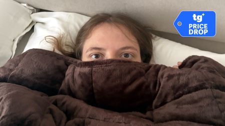 Sleep writer Ruth Jones lies wrapped up in the Oodie weighted blanket, a Tom's Guide price drop deals graphic in the top right corner