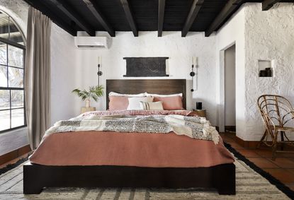 Mediterranean style bedroom with white walls, wood beams and bed with wood headboard 