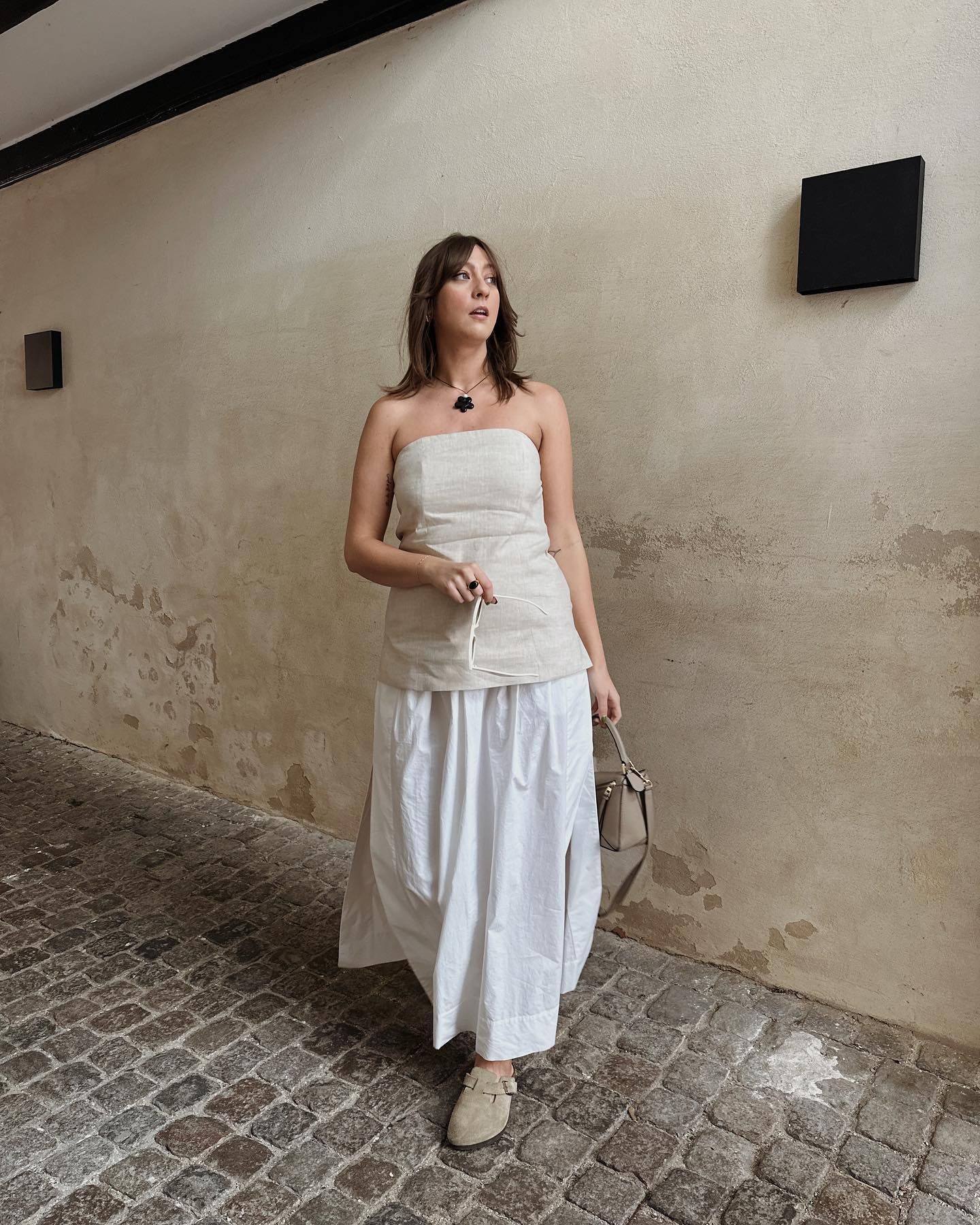 Woman on street wears beige bustier top, white skirt and beige sandals