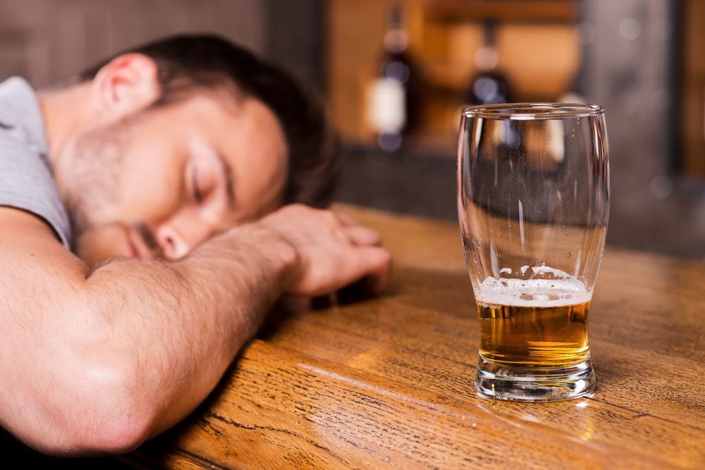 Drunk male customer leaning at the bar counter and sleeping with glass of beer in front of him.