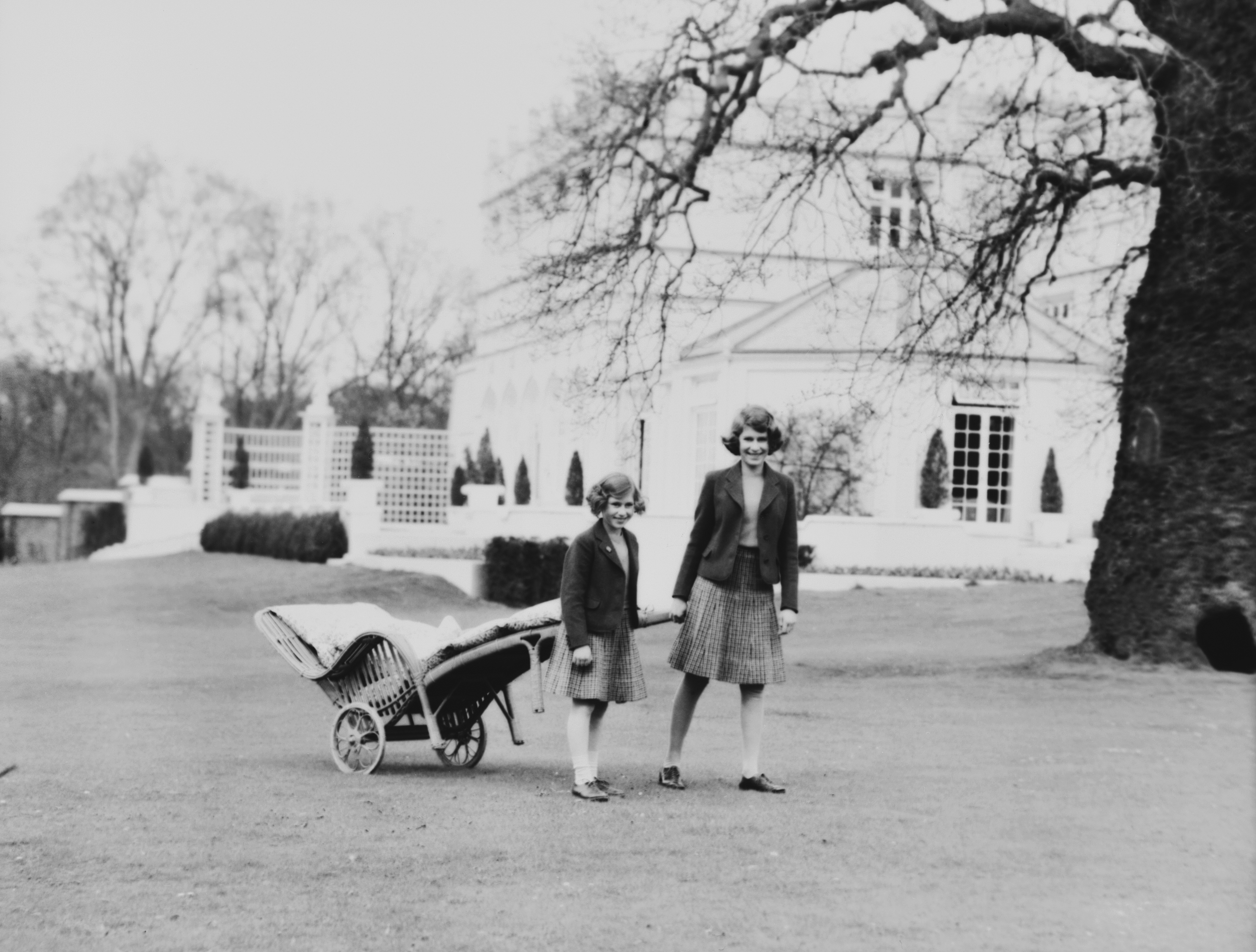 Queen Elizabeth and Princess Margaret pulling a wheelbarrow outside Royal Lodge