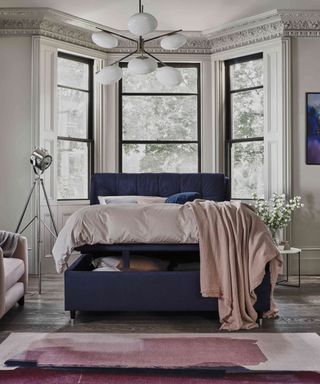 bedroom with navy velvet ottoman bed, blue and pink rug on wooden floor, pink throw on bed