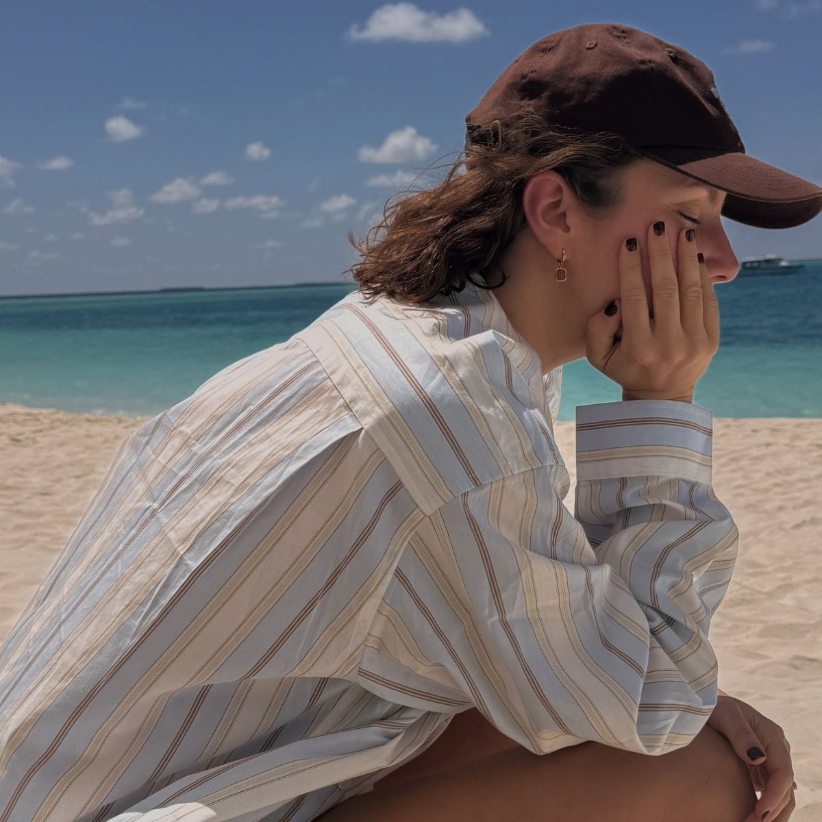Creator @emmahoareau sitting on the beach wearing a striped shirt and cap