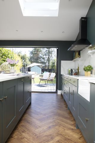 Open-plan kitchen diner with dark grey-green Shaker kitchen, parquet flooring and bifold doors out to a decked seating area