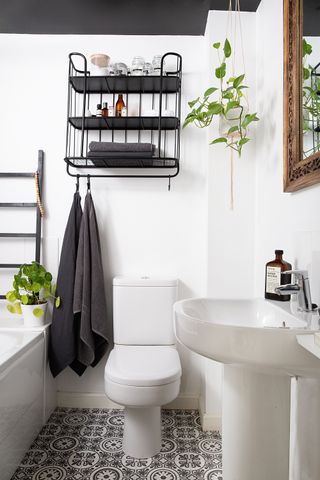 A white bathroom with black industrial-style shelving and a monochrome patterned vinyl floor