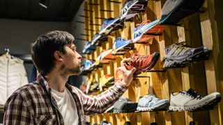 Man picks running shoe off shelf in shop