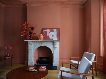 A living room painted in a smoky red shade with a fireplace and arm chairs
