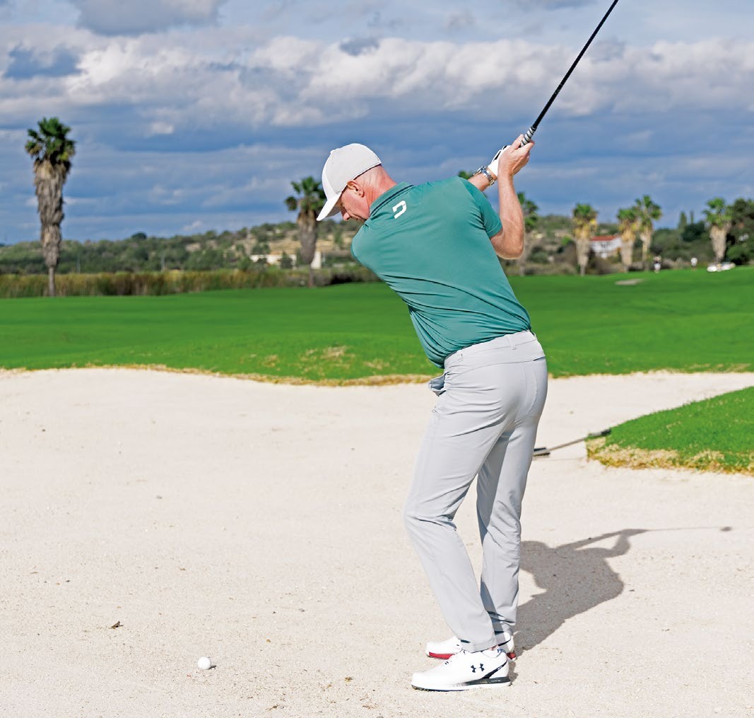 Ged Walters at the top of backswing with a hybrid in the fairway bunker