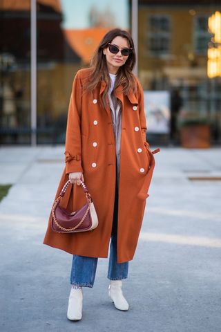 a woman wearing a long orange trench coat and straight leg jeans