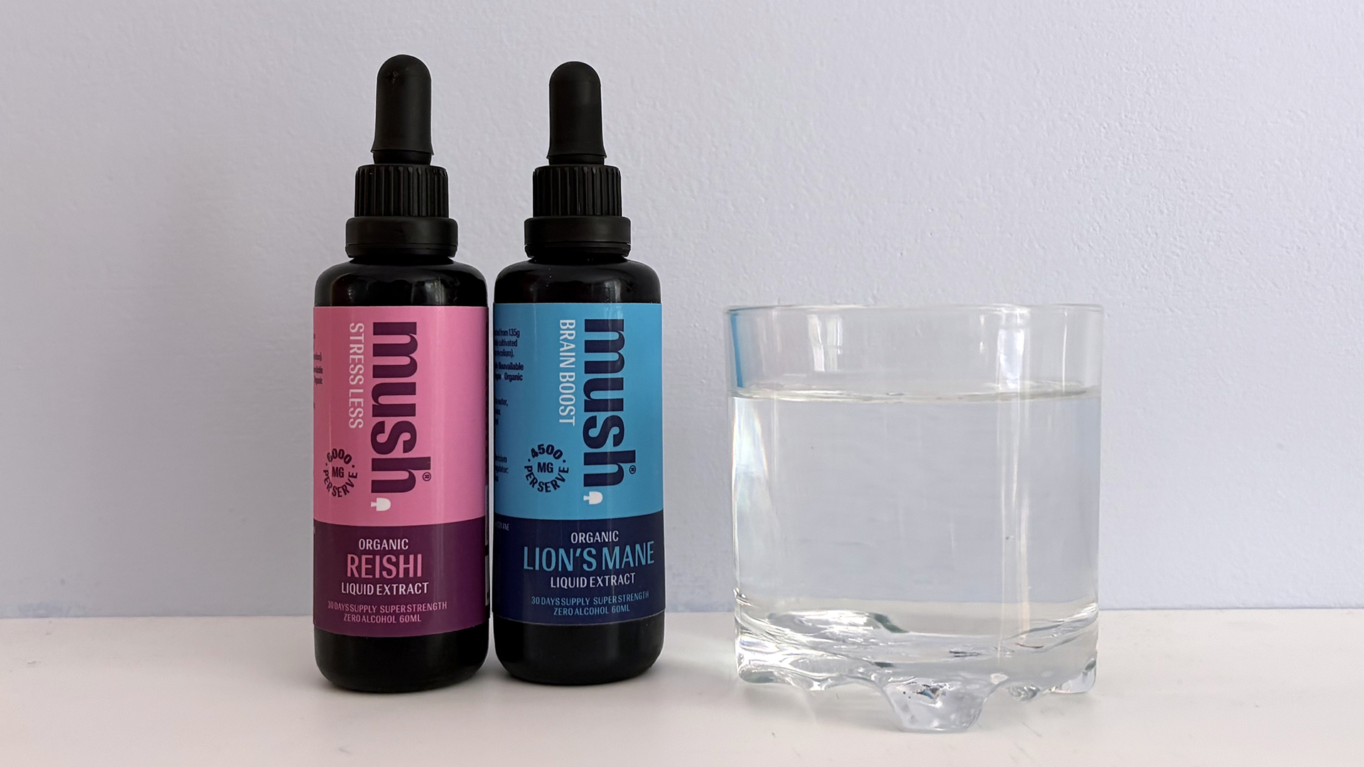 A close up of a bottle of Mush Reishi extract and Mush Lion's Mane extract next to a glass of water