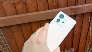 A white-backed Infinix Zero Ultra being held in a hand outside in a garden