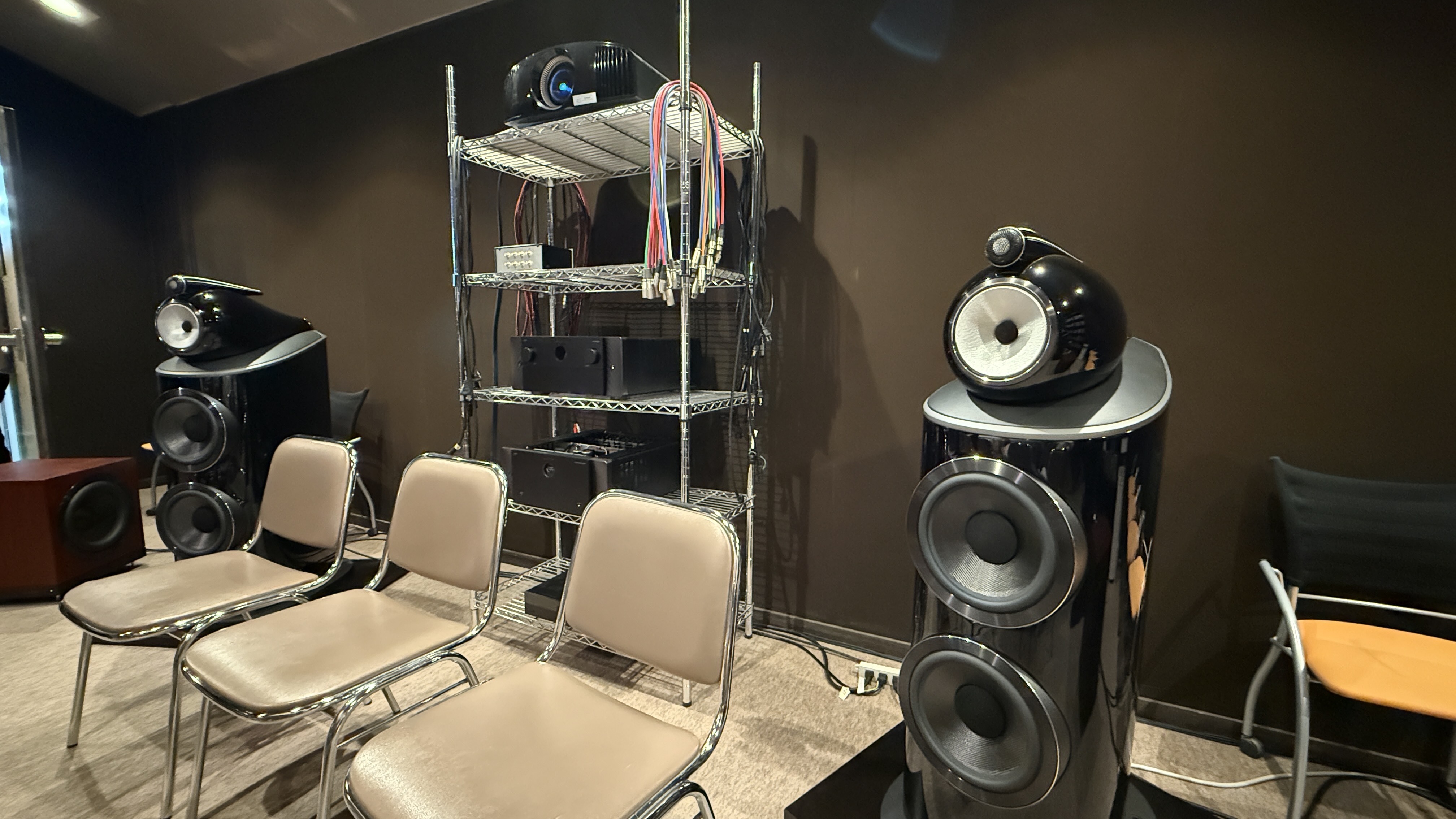 The interior of a home theater listening room with Bowers &amp; Wilkins 801 D4 speakers either side of a tall rack with a Sony projector on it