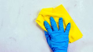 Waterproof blue glove with yellow cloth cleaning white wall