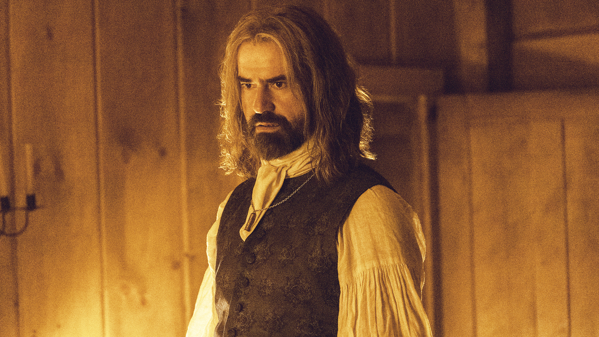 Richard Warren standing in a cabin room that's lit by candlelight in Widow's Bay episode 6