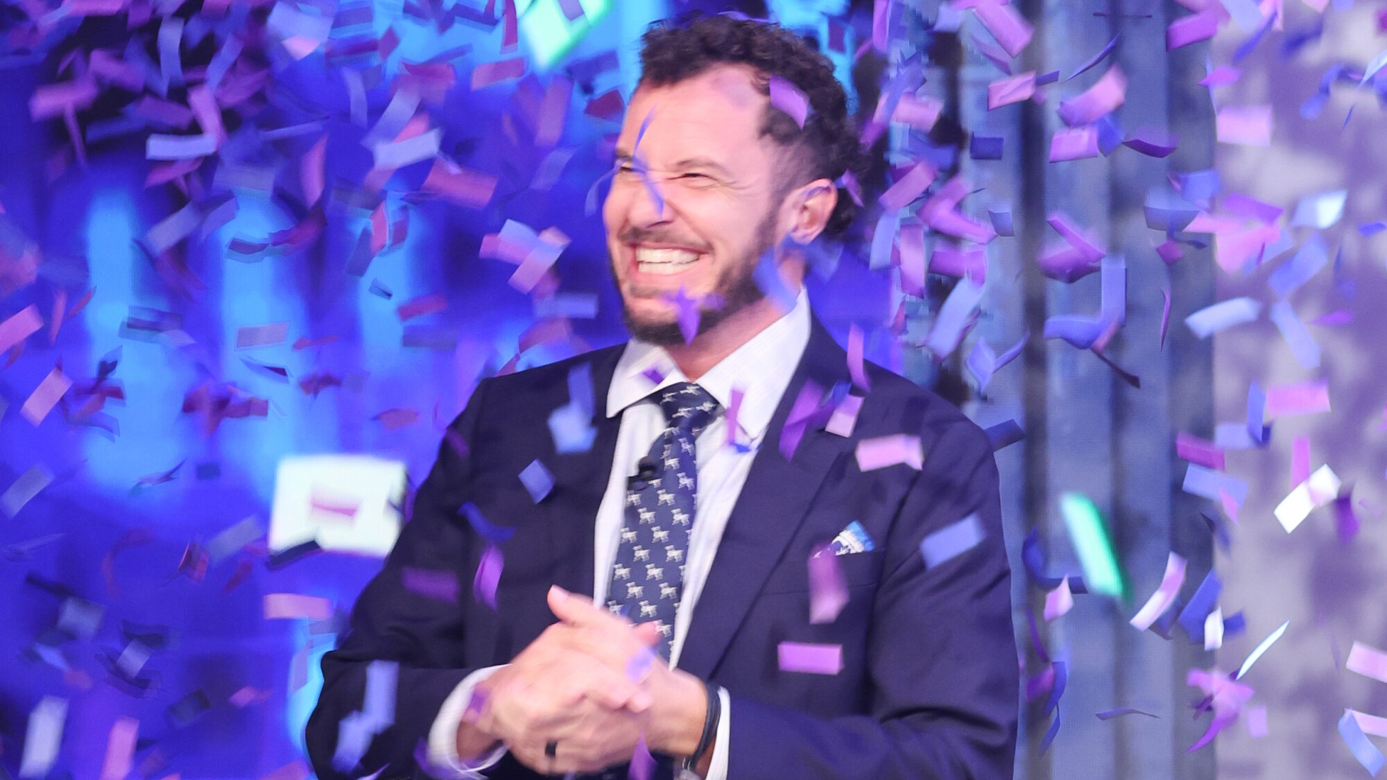 Rick Devens smiling as confetti rains down on him on the Big Brother stage. He's in a blue suit and tie with a white collared shirt. 