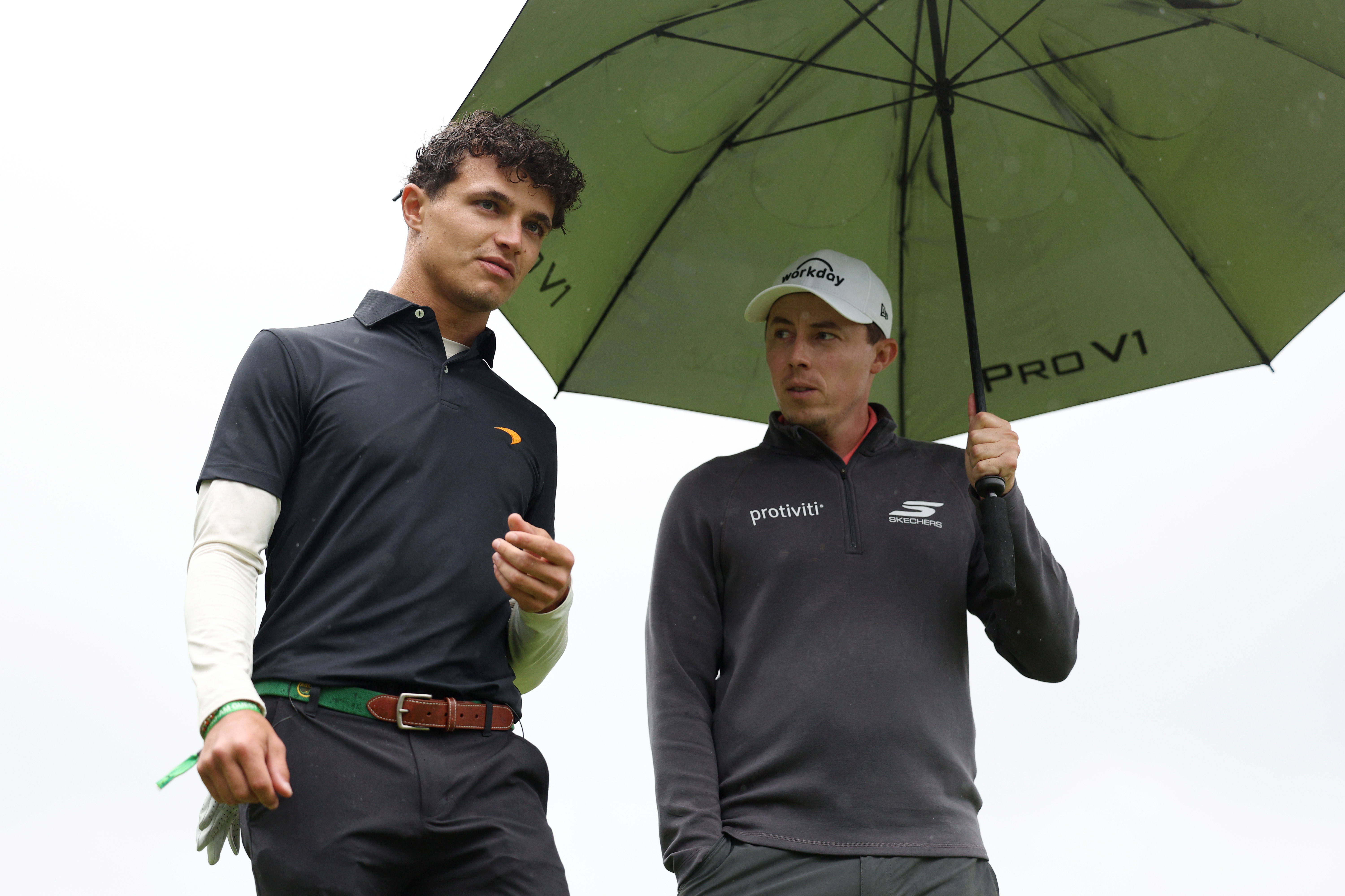 Lando Norris and Matt Fitzpatrick shelter under an umbrella