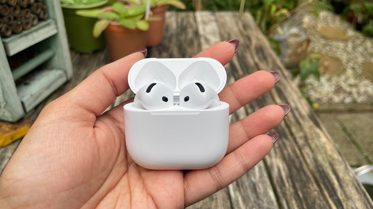 The Apple AirPods 4 with ANC in their case, held in front of a wooden outside surface.