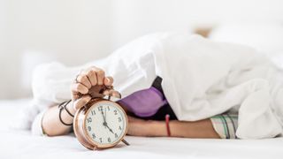 A woman under a duvet holding an alarm clock