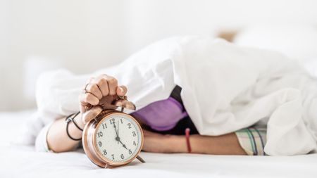 A woman under a duvet holding an alarm clock
