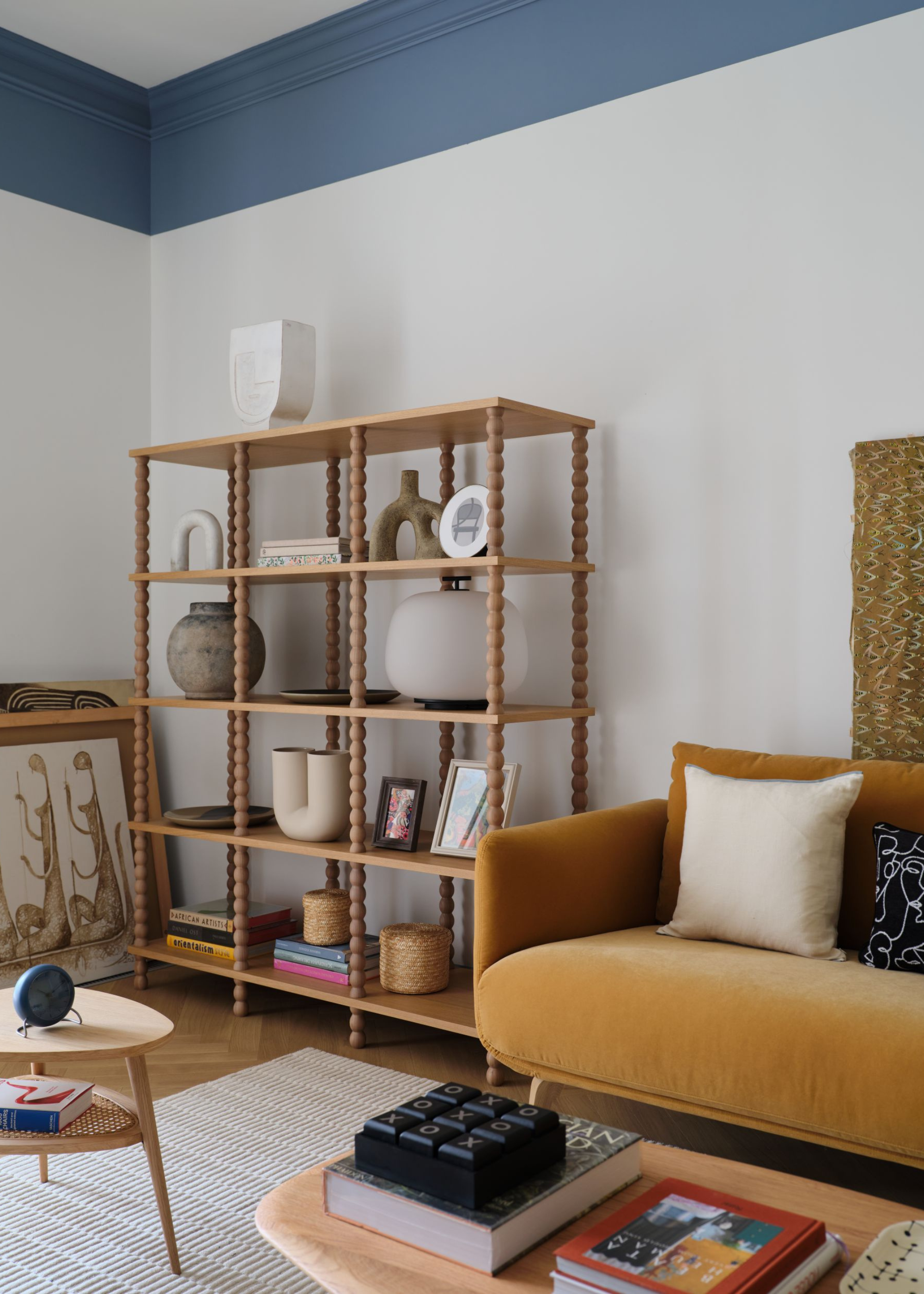 A mid-century design living room with a blue trimmed ceiling and open shelf cabinet with vases and art