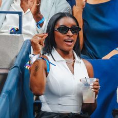 a woman with short black hair wearing a white top and black sunglasses at a sporting event