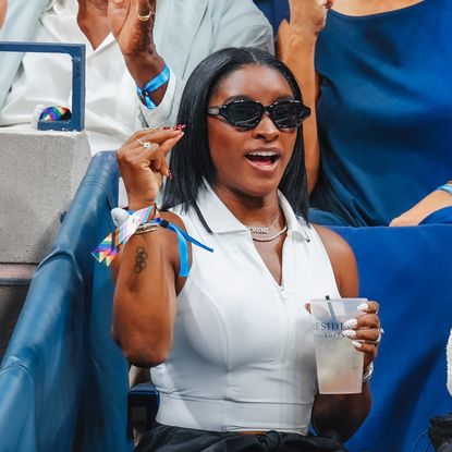 a woman with short black hair wearing a white top and black sunglasses at a sporting event