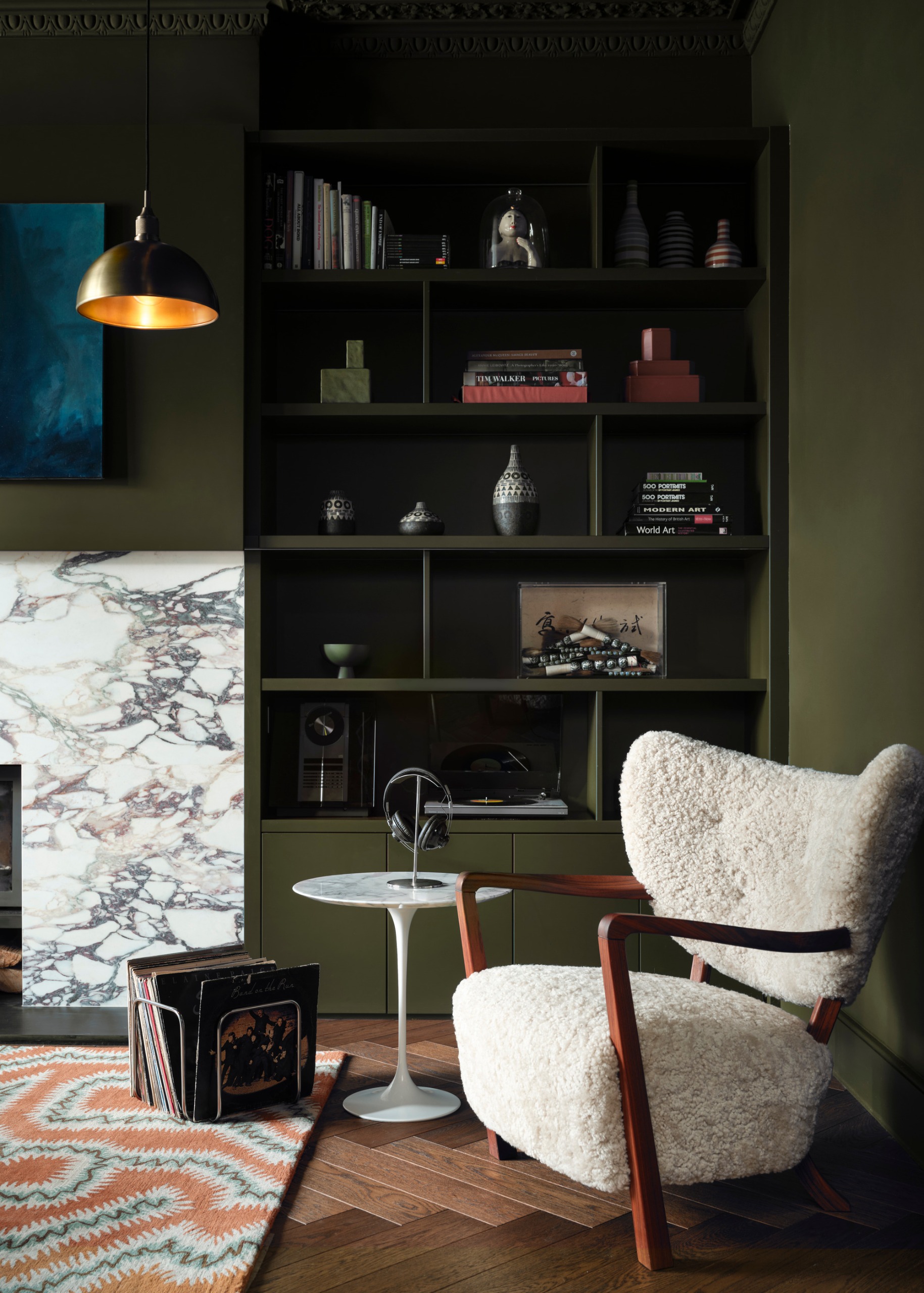 dark living room painted khaki green with fitted shelving and boucle chair