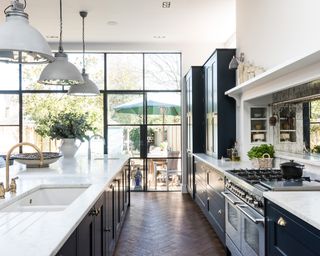 An example of open plan kitchen with large windows, marble counters and dark blue cabinetry.