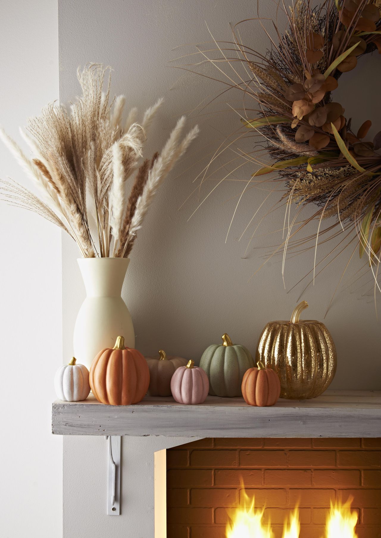 fall mantle with faux pumpkins, vase with dried flowers and autumnal wreath