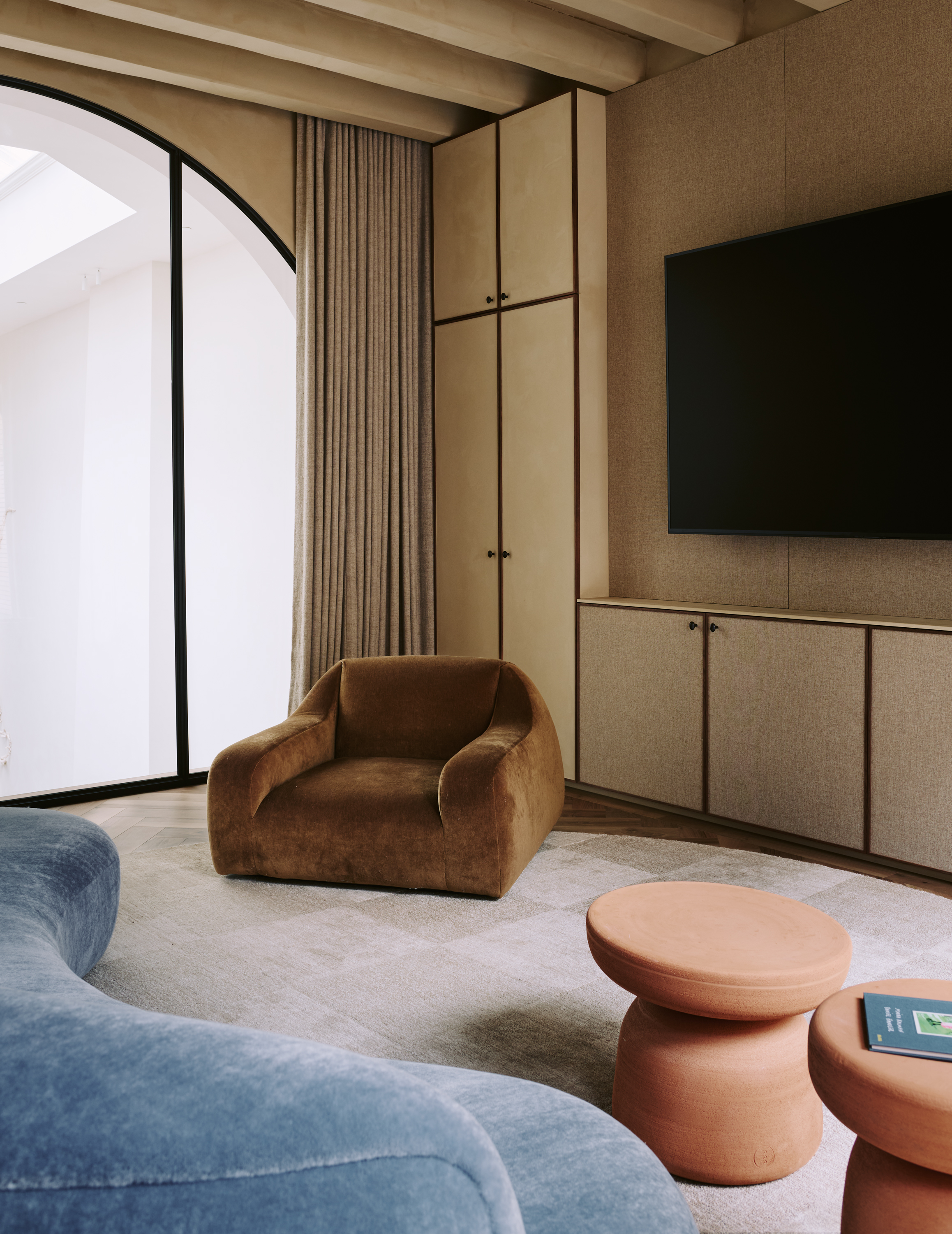 Image of a casual living room with fabric on the walls and cabinetry. There is a low light blue sofa, and a brown accent chair.