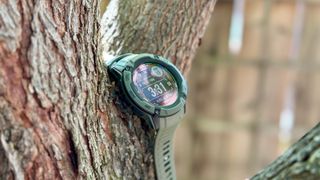 The Garmin Instinct 2X Solar hanging from a tree, showing the main watch face