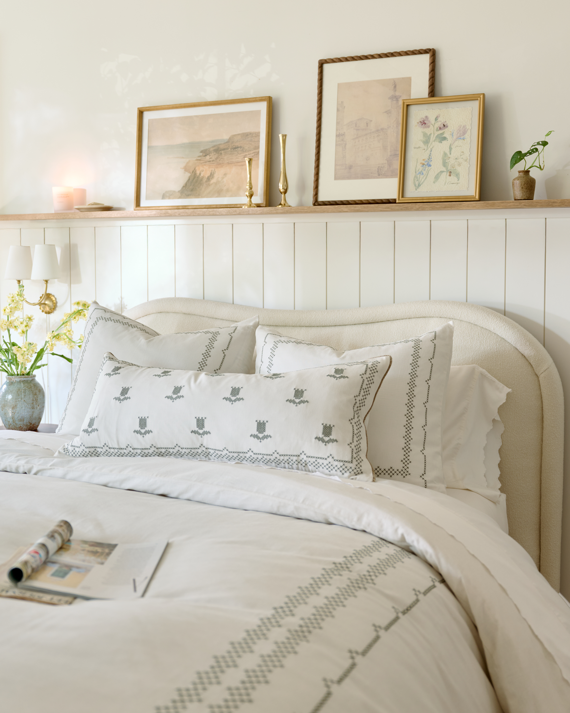 a white bedroom with white bedding and pictures on a rail above the bed