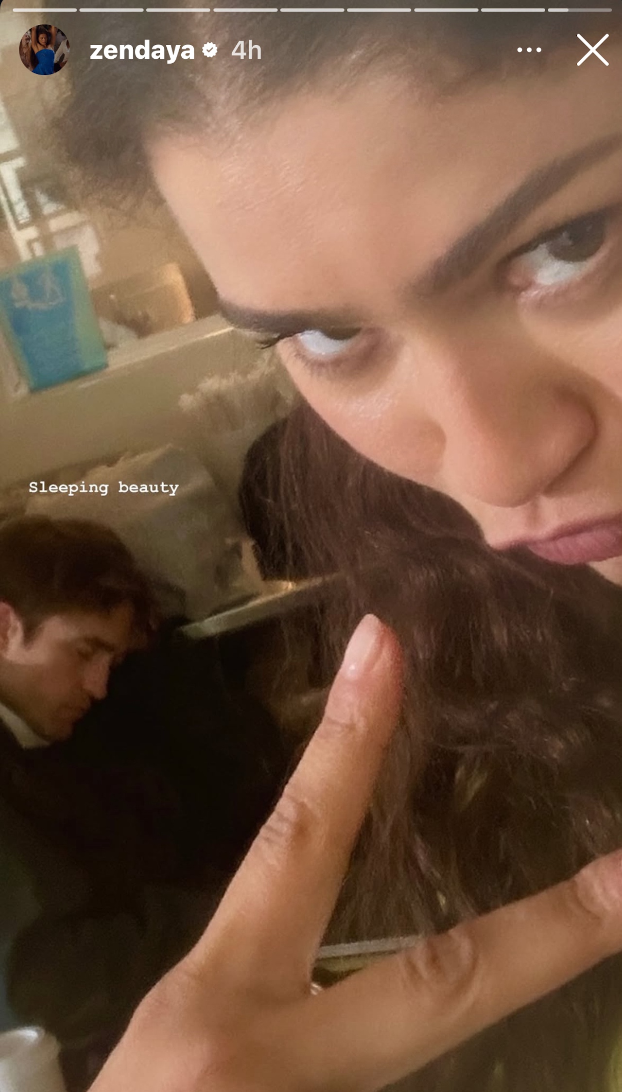 Zendaya throwing up a peace sign as Robert Pattinson sleeps in the background on The Drama set