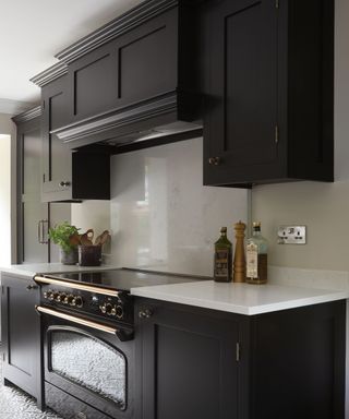 A kitchen with black wooden cabinets, a black stove with gold handles, and a white marble splashback