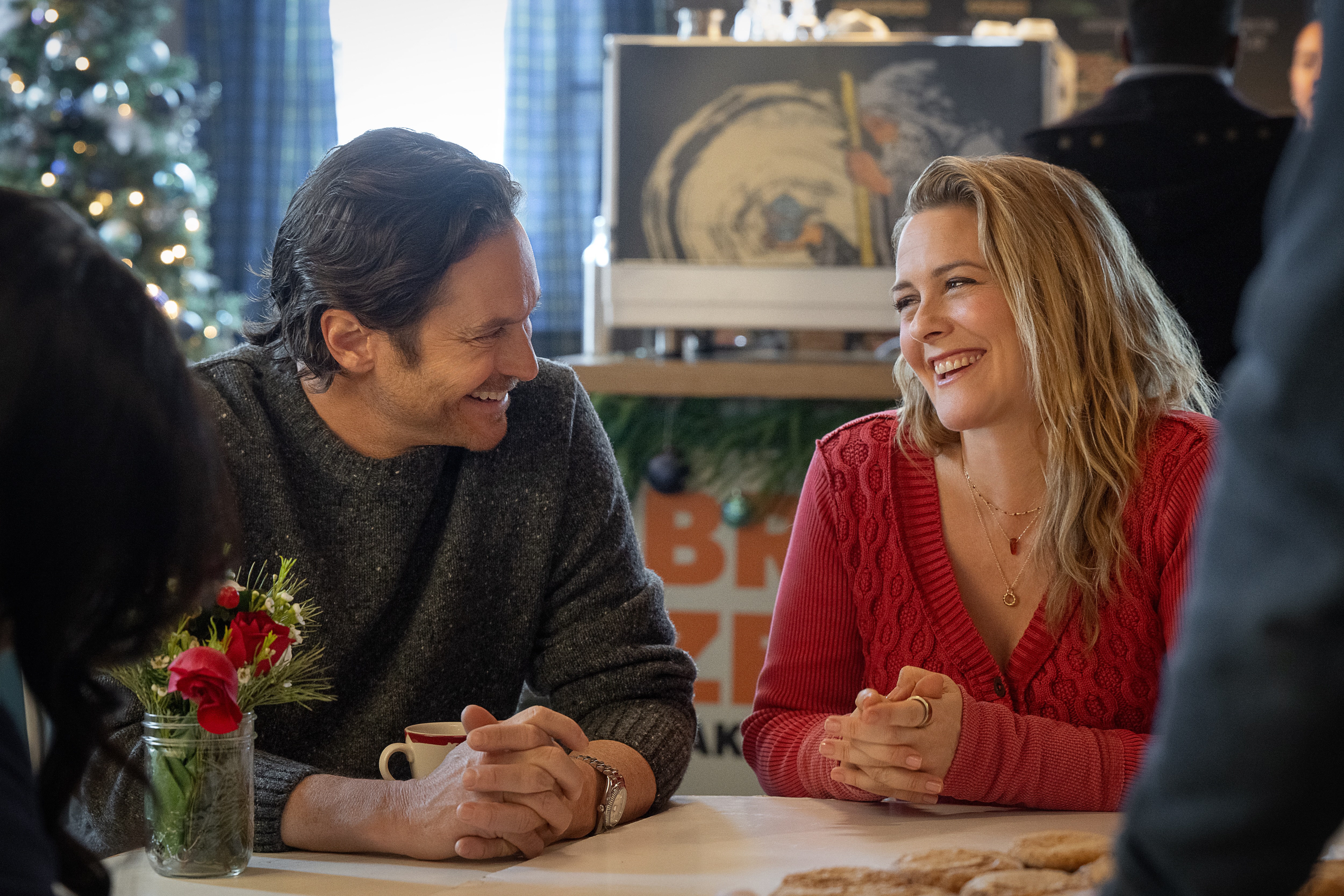 A Merry Little Ex-Mas. (L-R) Oliver Hudson as Everett and Alicia Silverstone as Kate smiling at each other over a dinner table with cookies on it in A Merry Little Ex-Mas