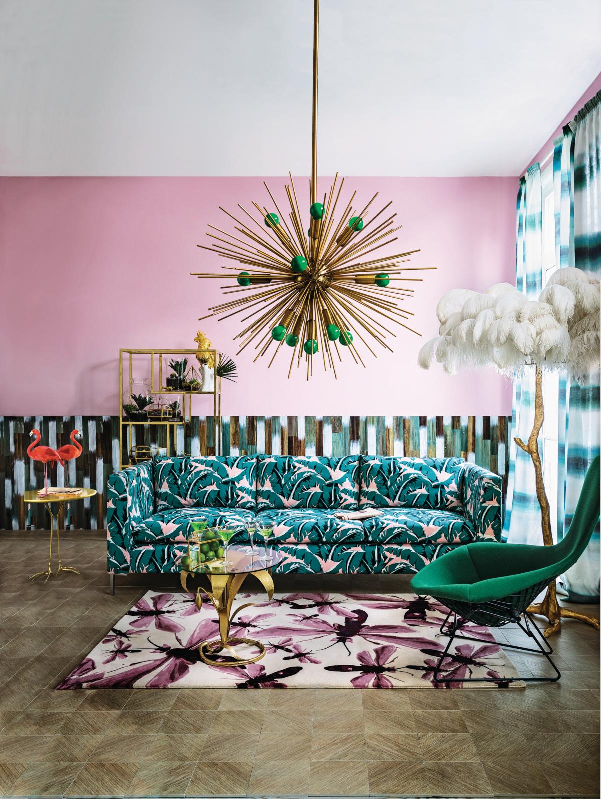 A maximalist living room painted bubble gum pink with different patterns all around the room. There is a tropical print sofa, a dragonfly rug, and tie-dye curtains.