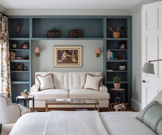 A large bedroom with sofa beneath built in bookshelves