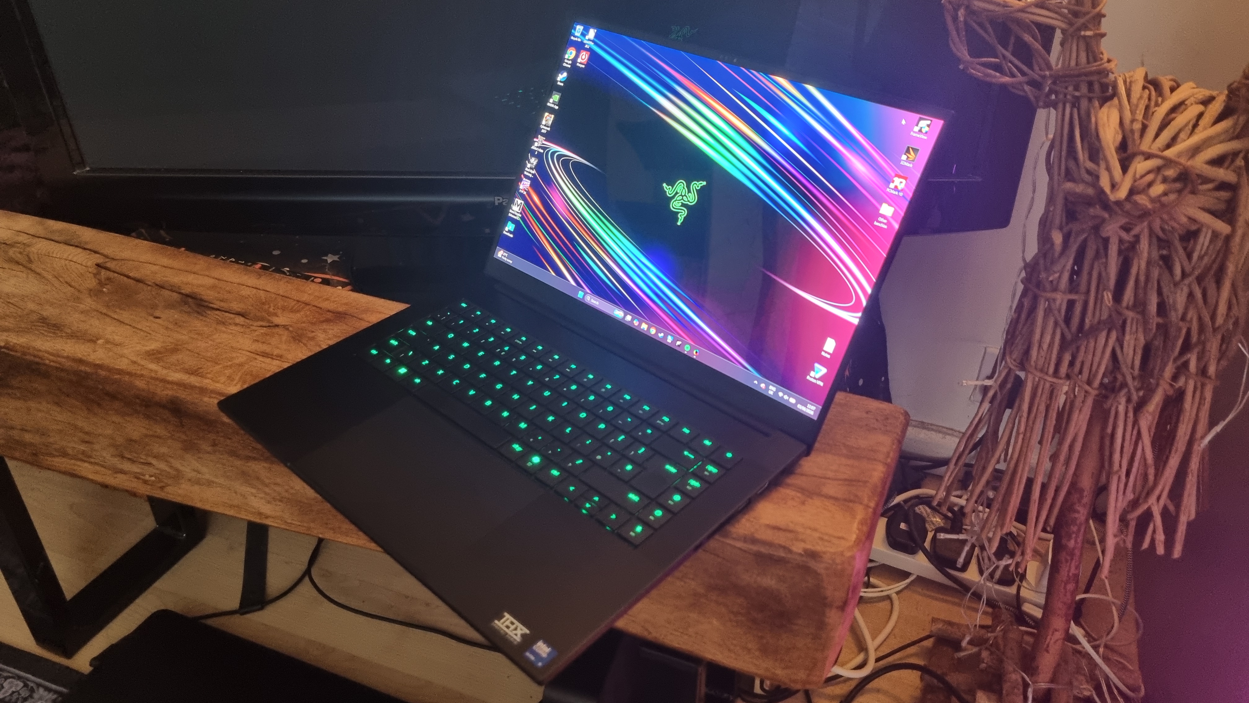 A Razer Blade 16 gaming laptop in front of a TV next to a wooden sculpture