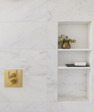 White tiled shower enclosure with recessed shelving, styled with brass vase and black soap dish