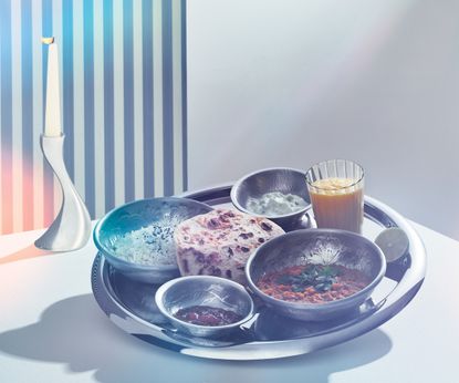 Five South Asian dishes on a silver tray with a candle on a table
