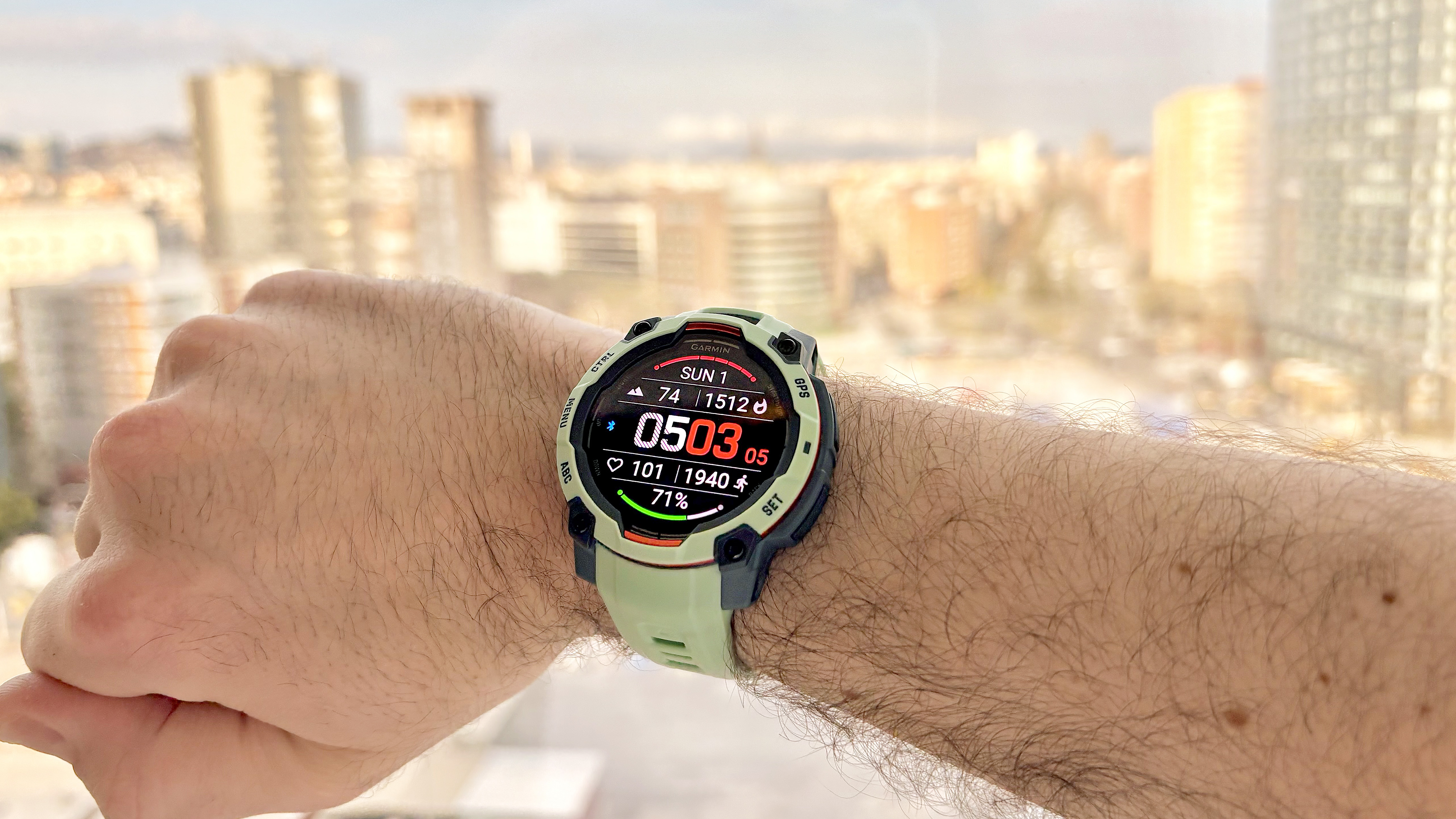 Close-up of the Garmin Instinct 3 on the writer's wrist with the Barcelona skyline out of focus in the distance