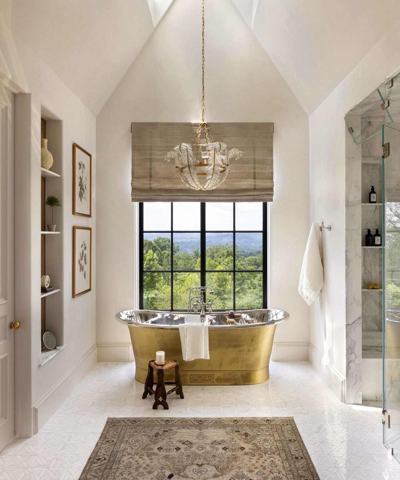 A tall, neutral bathroom with a brass freestanding bath and a patterned rug