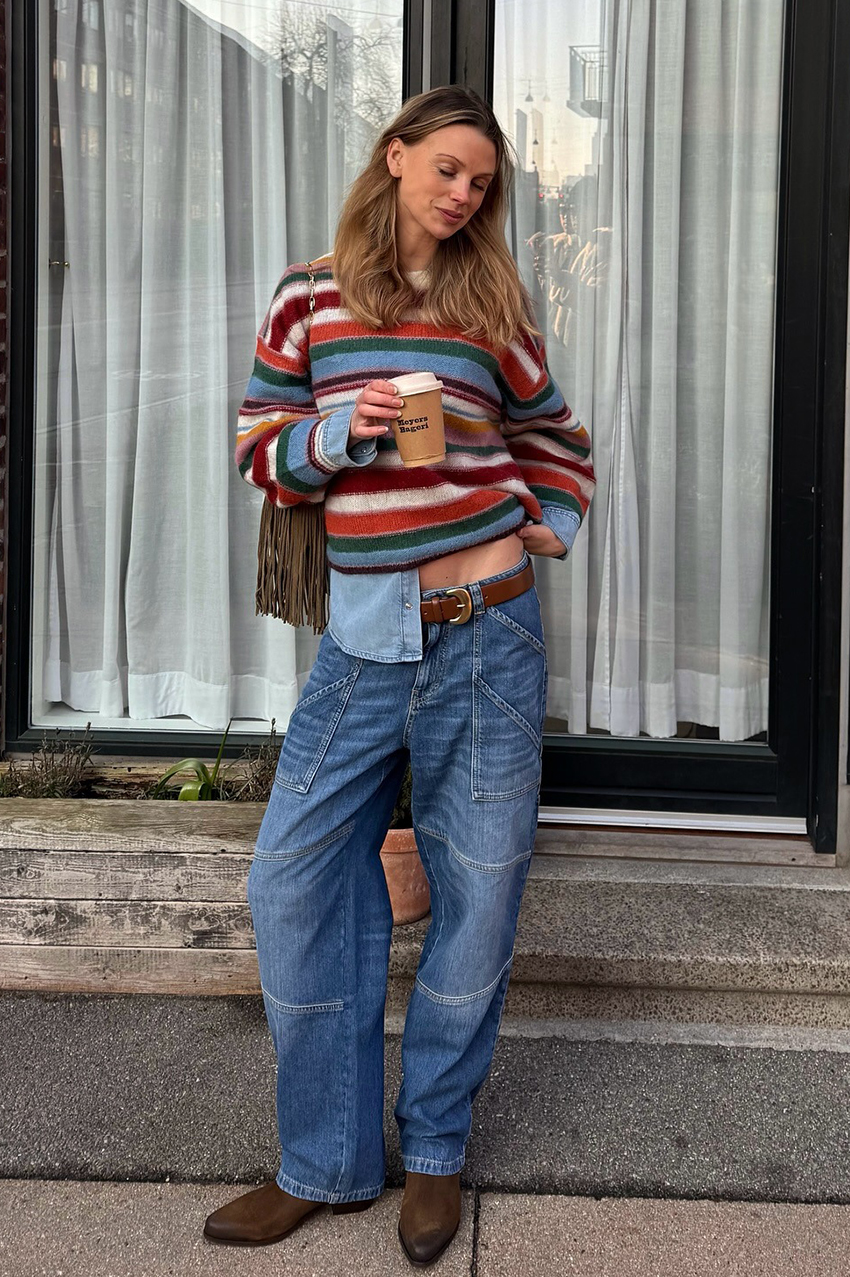 a woman wearing a striped sweater, blue baggy jeans, and pointed-toe brown boots