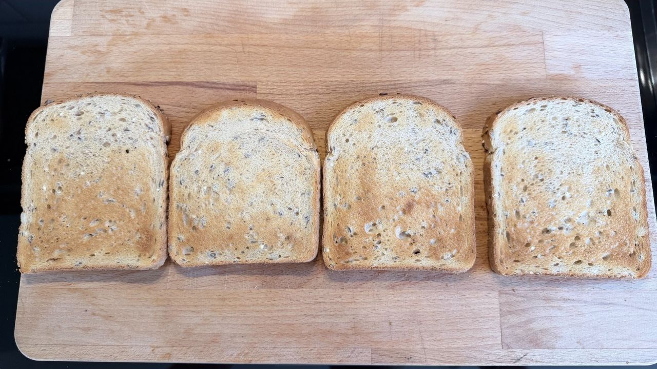 Four slices of toast on a wooden board after being cooked in the KitchenAid Pro Line toaster