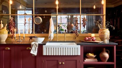 Landscape shot of red cabinets in kitchen with rustic look. It has a white fluted under-mounted butler sink, black counters, brass hanging rail and hardware